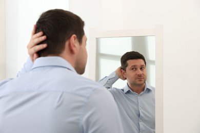 Photo of Handsome man looking at himself in mirror indoors
