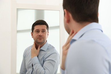 Photo of Handsome man looking at himself in mirror indoors