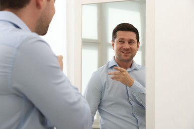 Photo of Handsome man looking at himself in mirror indoors