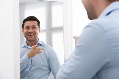 Photo of Handsome man looking at himself in mirror indoors