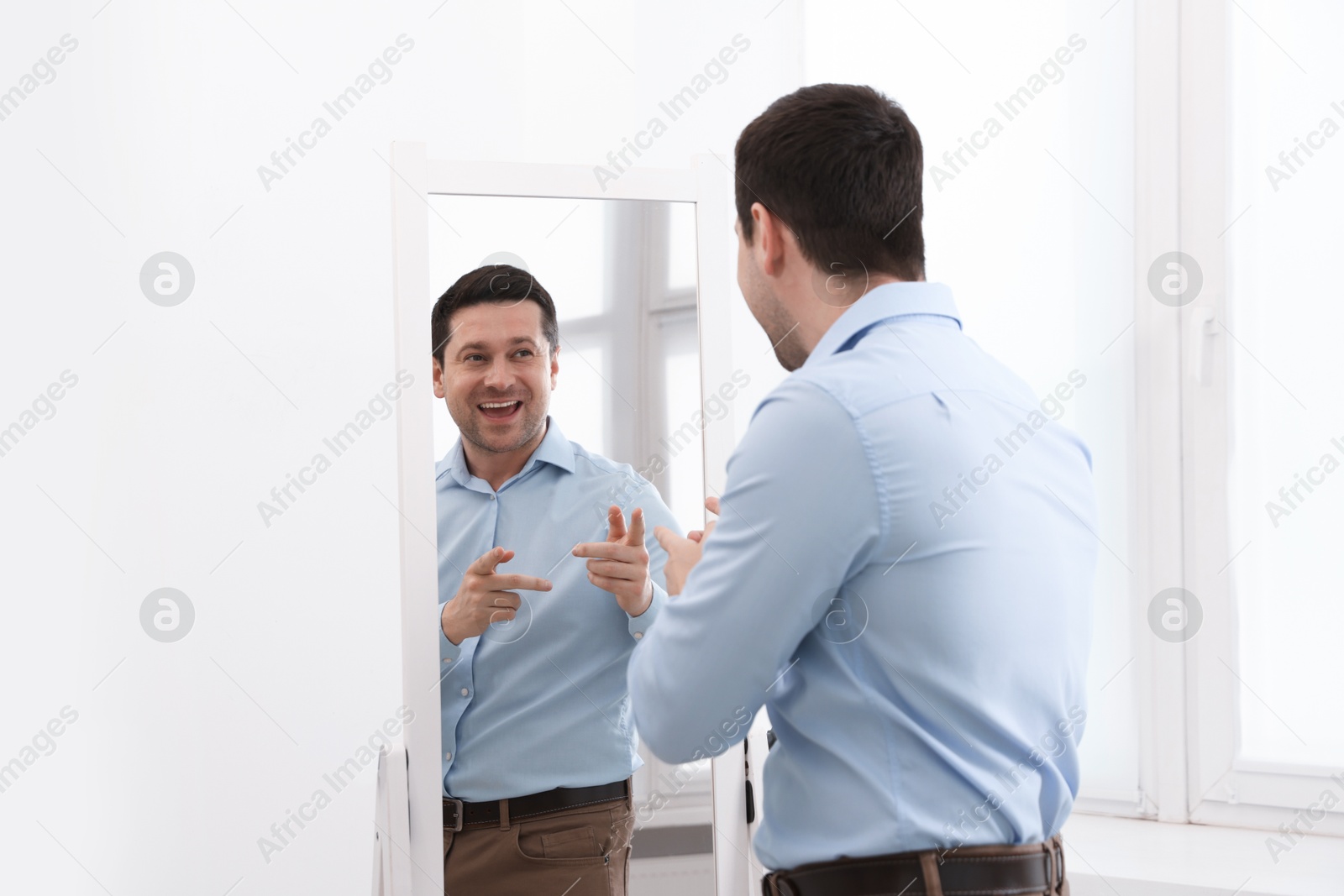 Handsome man looking at himself in mirror indoors Photo of Handsome man looking at himself in mirror indoors