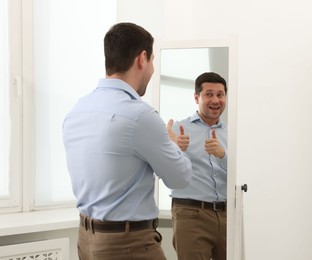 Photo of Handsome man showing thumbs up near mirror indoors