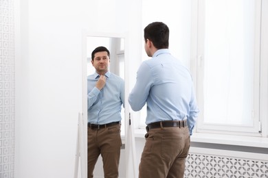 Photo of Handsome man looking at himself in mirror indoors