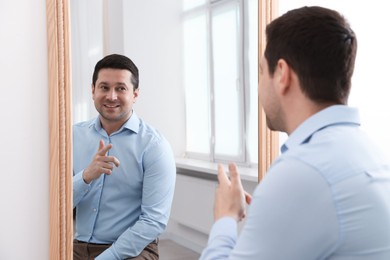 Photo of Handsome man looking at himself in mirror indoors