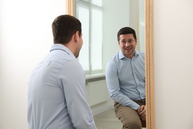 Photo of Handsome man looking at himself in mirror indoors