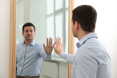 Photo of Handsome man looking at himself in mirror indoors