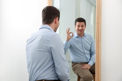 Photo of Handsome man showing ok gesture near mirror indoors