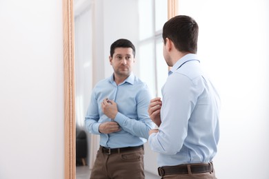 Photo of Handsome man looking at himself in mirror indoors