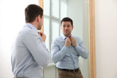 Photo of Handsome man looking at himself in mirror indoors