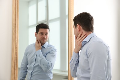 Photo of Handsome man looking at himself in mirror indoors