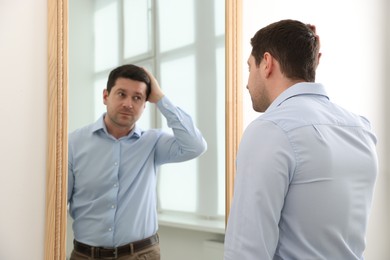 Photo of Handsome man looking at himself in mirror indoors