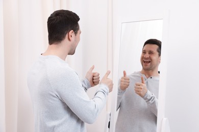 Photo of Handsome man showing thumbs up near mirror indoors