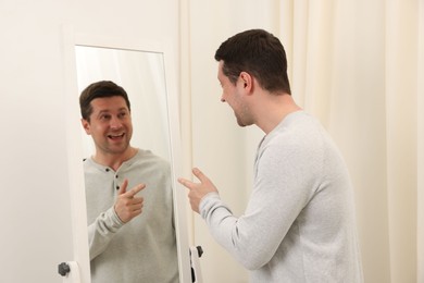 Photo of Handsome man looking at himself in mirror indoors