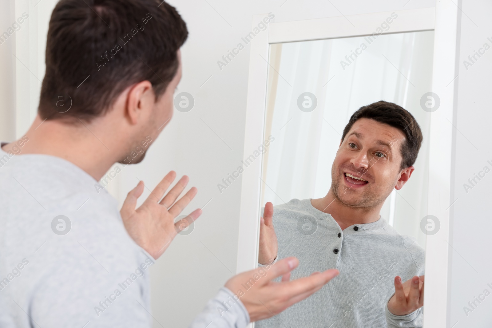 Handsome man looking at himself in mirror indoors Photo of Handsome man looking at himself in mirror indoors