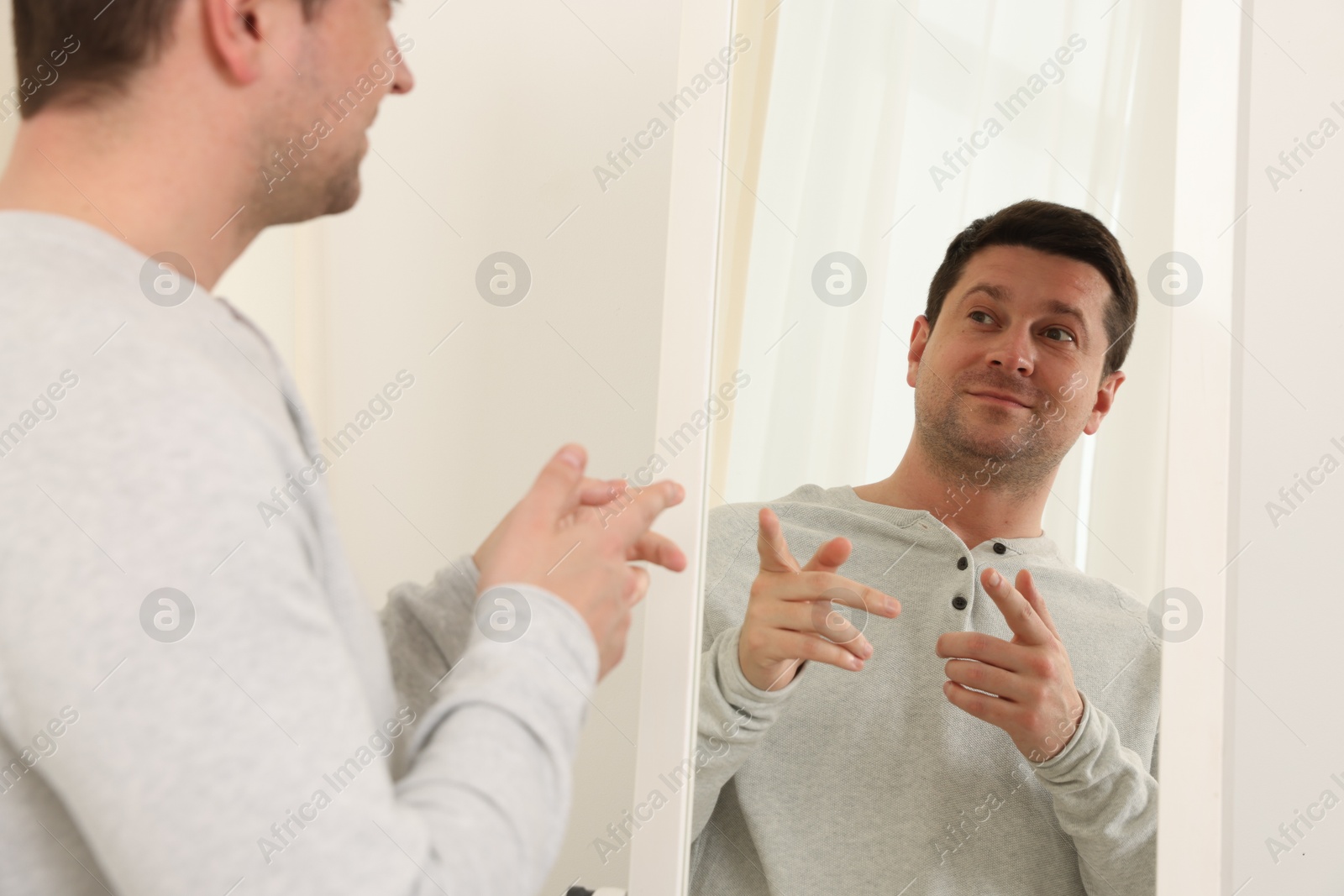 Handsome man looking at himself in mirror indoors Photo of Handsome man looking at himself in mirror indoors