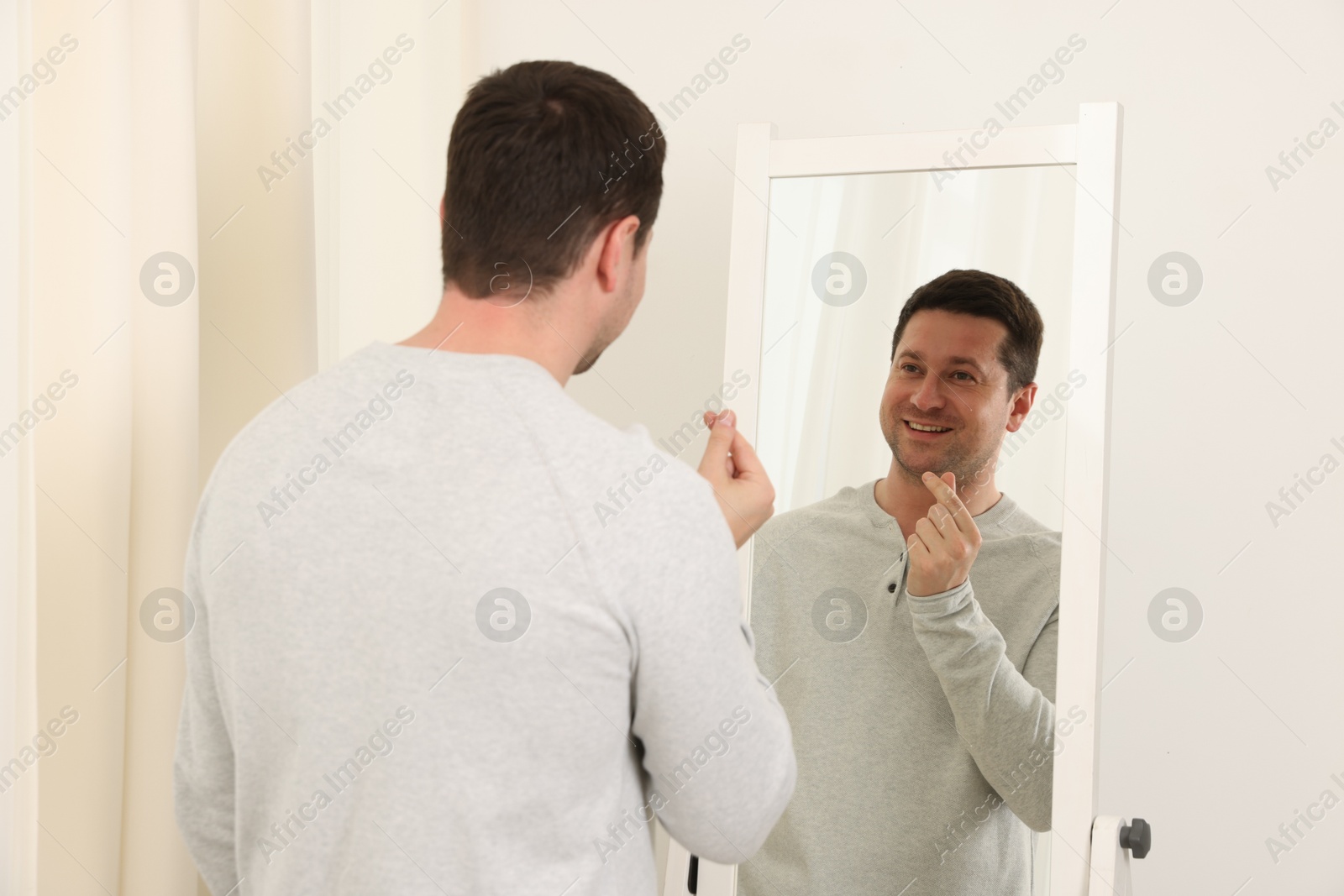 Handsome man showing heart gesture near mirror indoors Photo of Handsome man showing heart gesture near mirror indoors