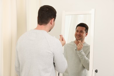 Photo of Handsome man showing heart gesture near mirror indoors
