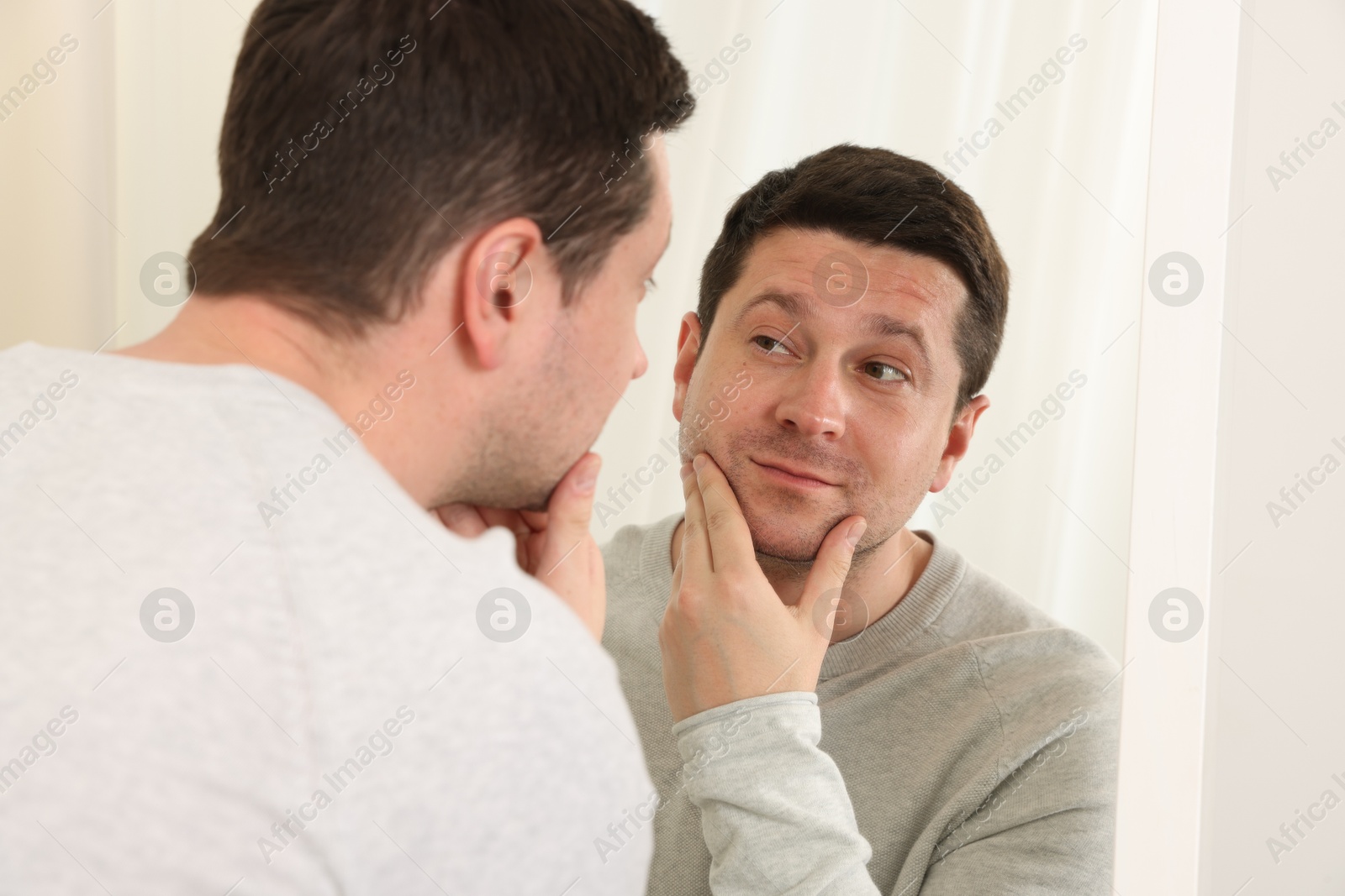 Handsome man looking at himself in mirror indoors Photo of Handsome man looking at himself in mirror indoors