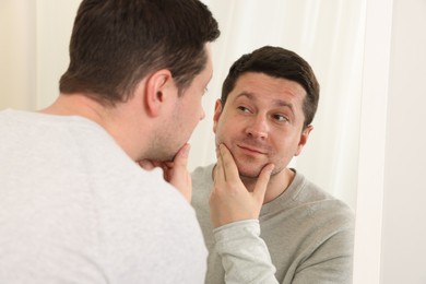 Photo of Handsome man looking at himself in mirror indoors