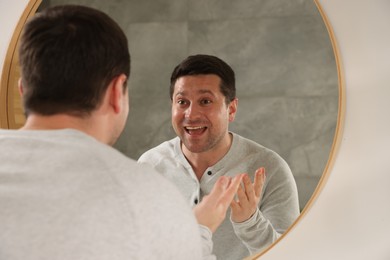 Photo of Handsome man looking at himself in mirror indoors