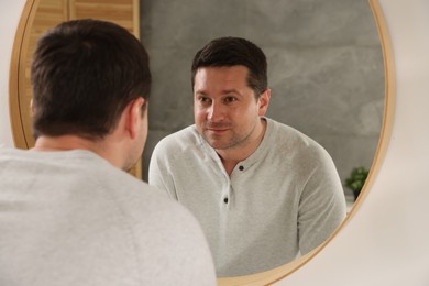 Photo of Handsome man looking at himself in mirror indoors