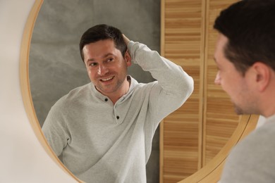 Photo of Handsome man looking at himself in mirror indoors