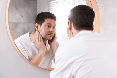Photo of Handsome man looking at himself in mirror indoors