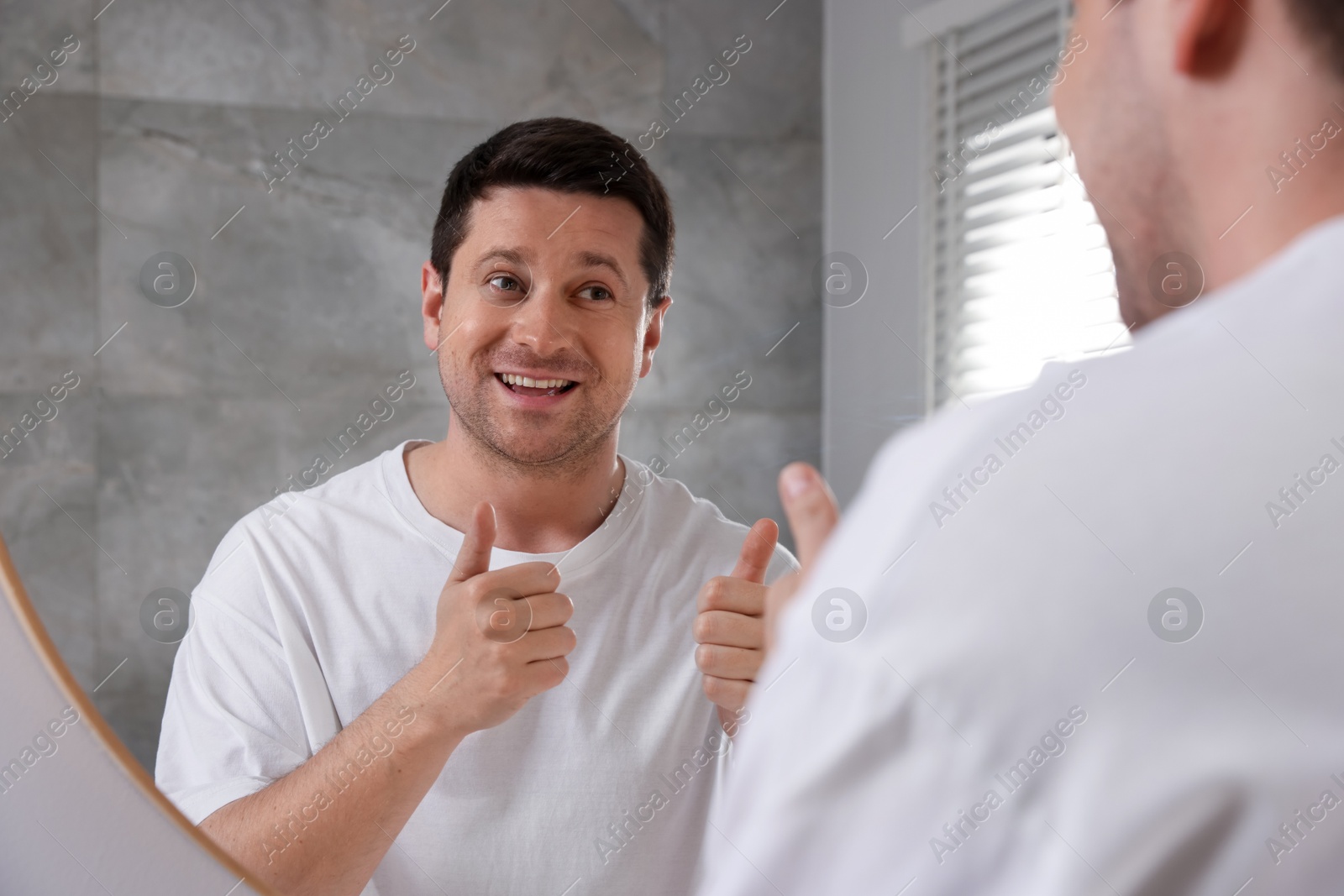 Handsome man showing thumbs up near mirror indoors Photo of Handsome man showing thumbs up near mirror indoors