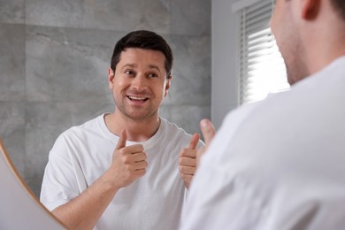 Photo of Handsome man showing thumbs up near mirror indoors