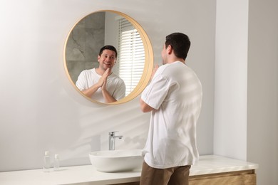 Photo of Handsome man looking at himself in mirror indoors