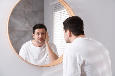 Photo of Handsome man looking at himself in mirror indoors