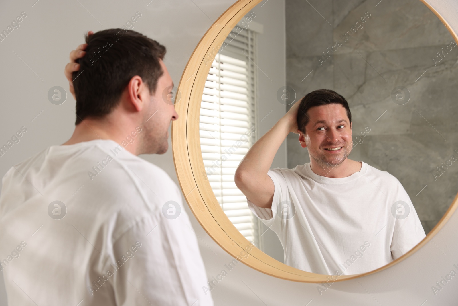 Handsome man looking at himself in mirror indoors Photo of Handsome man looking at himself in mirror indoors