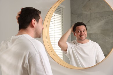 Photo of Handsome man looking at himself in mirror indoors