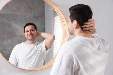Photo of Handsome man looking at himself in mirror indoors