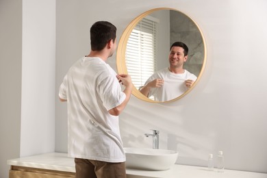 Photo of Handsome man looking at himself in mirror indoors