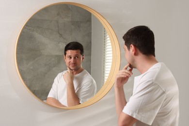 Photo of Handsome man looking at himself in mirror indoors