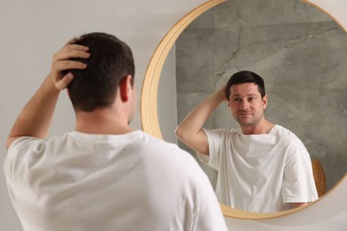 Photo of Handsome man looking at himself in mirror indoors