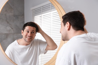 Photo of Handsome man looking at himself in mirror indoors