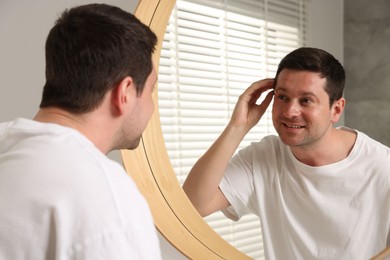Photo of Handsome man looking at himself in mirror indoors