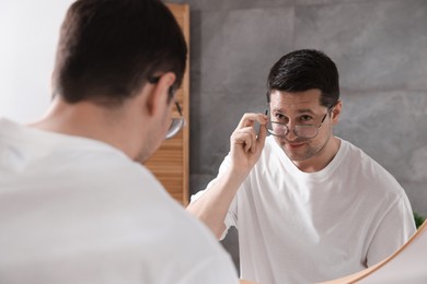Photo of Handsome man looking at himself in mirror indoors