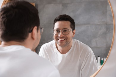 Photo of Handsome man looking at himself in mirror indoors