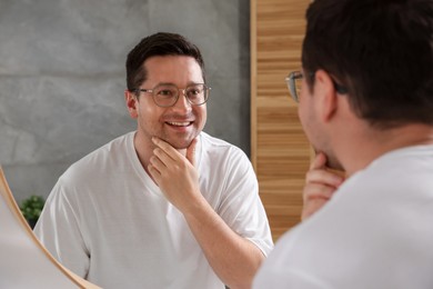 Photo of Handsome man looking at himself in mirror indoors
