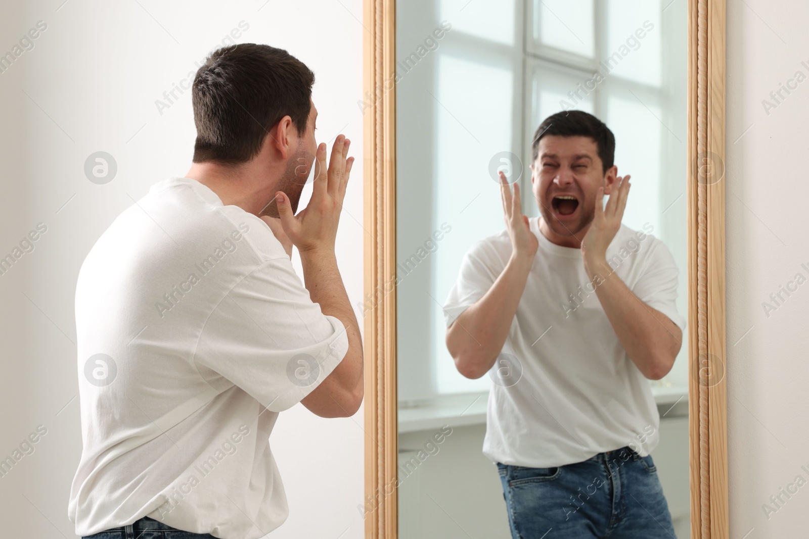 Handsome man looking at himself in mirror indoors Photo of Handsome man looking at himself in mirror indoors