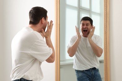 Photo of Handsome man looking at himself in mirror indoors