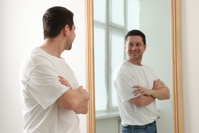 Photo of Handsome man looking at himself in mirror indoors