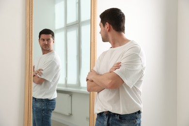 Photo of Handsome man looking at himself in mirror indoors
