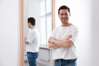Photo of Handsome man with crossed arms near mirror indoors