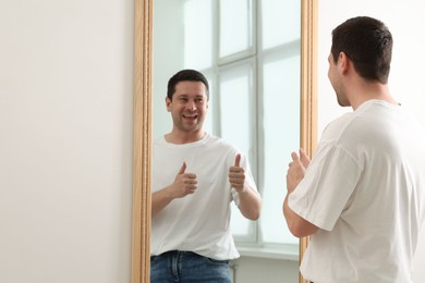 Photo of Handsome man showing thumbs up near mirror indoors, space for text