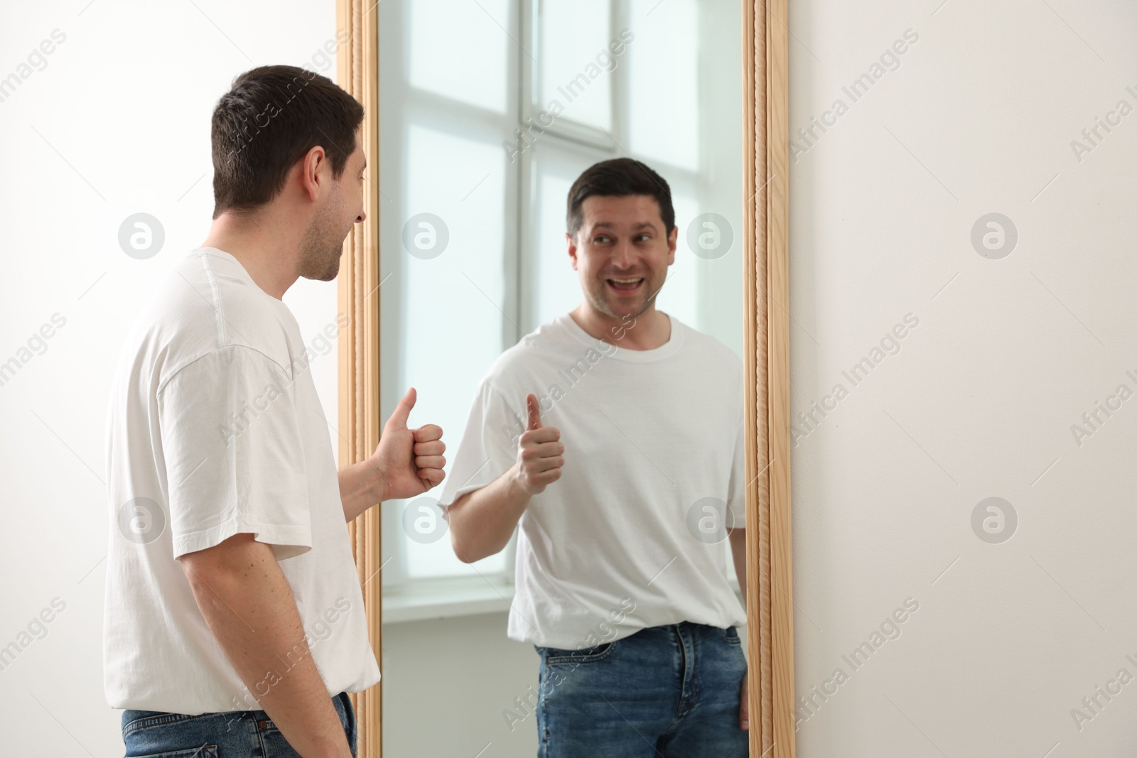 Handsome man showing thumbs up near mirror indoors Photo of Handsome man showing thumbs up near mirror indoors