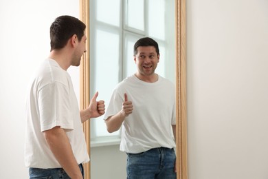 Photo of Handsome man showing thumbs up near mirror indoors